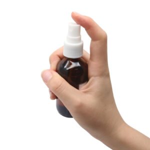 Hand pressing the white spray nozzle on an amber hair care bottle.