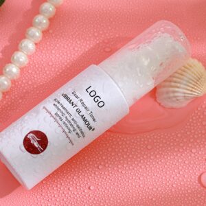 Clear skincare toner bottle on pink fabric beside pearls and a shell.