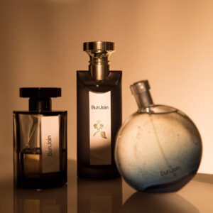 Three perfume bottles in amber and gold tones on a reflective surface.