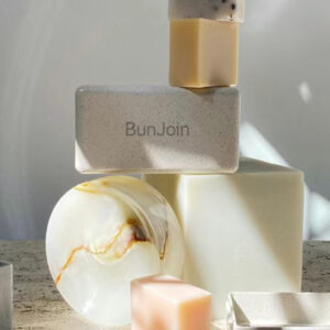 Shaving soap bars, a soap dish and a BunJoin bottle on a stone surface.