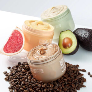 Three open body scrub jars displayed with coffee beans, grapefruit and avocado.
