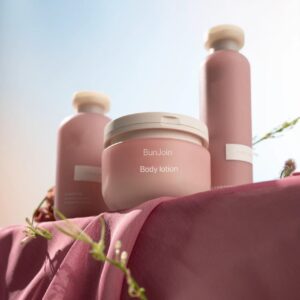 Pink body lotion bottles and jar displayed on draped fabric.