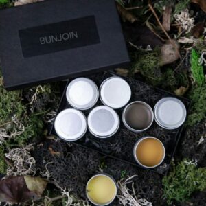 Open and closed solid cologne tins beside a black BunJoin gift box.