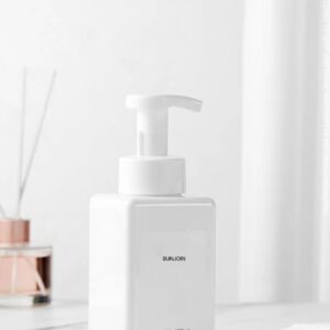 White rectangular hand soap pump bottle beside a towel and reed diffuser.