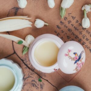 Open floral solid perfume jar surrounded by jasmine flowers.
